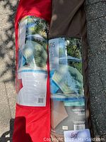Photo of two rolled outdoor umbrellas with protective carry bags, one red and one mocha, showing product labels and carrying handles.