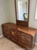 Front view of a wooden dresser with multiple drawers and attached rectangular mirror in a bedroom setting.