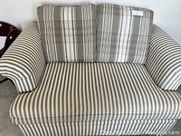 Front view of the loveseat showing striped fabric seat and plaid cushions in beige and grey tones.
