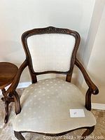 Full view of the carved wood armchair showing offwhite fabric upholstery on seat and backrest, with carved wood arms and frame.