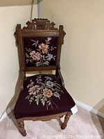 Front view of Victorian carved wood chair with burgundy needlepoint upholstery showing floral embroidery.