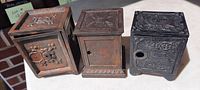 Photo showing three antique cast steel banks with detailed exterior designs, various designs and patinas visible on each bank.