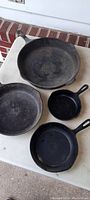 Top view of 4 cast iron pans showing size difference, surface wear, and seasoning.