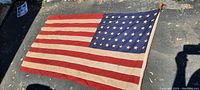 Full view of the 48 star American flag with attached wooden pole laid flat showing entire flag design and pole.