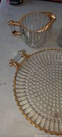 Close-up of vintage small glass pitcher with gold rimmed handle and spout, and ribbed glass design