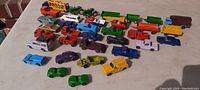 A photo showing 35 small metal vehicles of various types and colors arranged on a flat surface, including cars, trucks, tractors, construction toys, trailers, and sports cars mostly Matchbox size or smaller.