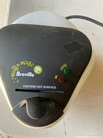 Top view of closed Breville Muffin Magic appliance with brand name, caution label, and indicator lights visible.