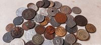 Photo shows approximately 40 assorted antique foreign coins laid out showing varied sizes, colors, and metal compositions including copper, bronze, and silver tones. Many coins show wear and patina, some feature holes in the center.