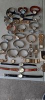 Full view of 28 wristwatches arranged on a flat surface, showing varied styles and band materials