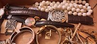 Photo showing watches, white beaded necklace and enamel pin with black and white Maltese cross
