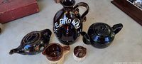 Overview photo showing dark brown ceramic Little Brown Jug music box and vintage dark brown glass teapots and servers