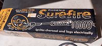 Box showing vintage branding and product name Phoenix Surefire, notes it ignites charcoal and logs electrically.