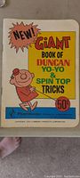 Front cover of booklet titled 'New! Giant Book of Duncan Yo-Yo & Spin Top Tricks' with cartoon character and 1973 copyright by Flambeau Products Corporation.