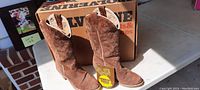 Pair of brown Wolverine cowboy boots with original box behind them, tags visible on the boots