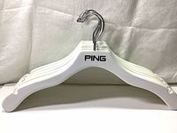 Stack of white wooden hangers with PING logo and silver metal hooks, showing slim, durable design and shoulder grooves.