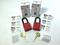 Two new red Master Lock safety padlocks with keys, lockout tags, instruction sheets, and original boxes arranged on a white surface.