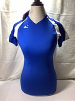 Front view of royal blue athletic shirt with white shoulder accents on dress form, showing Mizuno logo on chest and V-neck style.