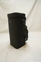 Front-side view of the black padded lens case with adjustable strap attached and zipper lid visible.