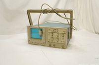 Front left angle view of Tektronix TAS 465 oscilloscope showing CRT screen, carrying handle and power cable draped over screen.