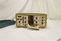Front and partial top view of the Tektronix TM 515 oscilloscope with open panel showing controls and components.