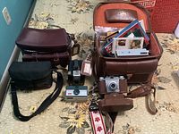 Overview of multiple vintage cameras, cases and manuals on a floral patterned surface.