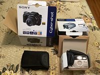 Sony Cyber-shot DSC-H10 box, Sony Handycam box, Minolta F35 Big Finder camera in case and box on table