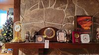 Wide view of multiple clocks on a stone mantle, including a glass dome clock, rectangular wooden clock, and several small alarm clocks.