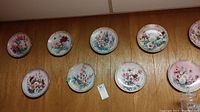 First photo showing 10 floral collector plates mounted on a wooden wall, showcasing various pastel floral designs.