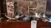 Front view of assorted animal figurines including shark, whale, lobster hanging, seagull, and bird on branch displayed on wood surface.