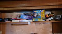 Photo showing shelf with several board games including ProjectaScope, Balderdash, Monopoly, and others with visible titles and boxes.