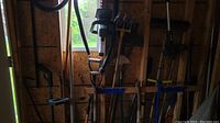 Wide view showing several garden tools hanging on pegboard wall including shovels, a manual sod cutter, a hand cultivator, and other hand tools
