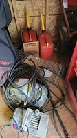Photo showing two red gas cans with yellow spouts, a power cord, electric pressure washer, and metal animal crate.