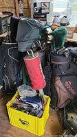 Three golf bags with clubs and a yellow bin of accessories