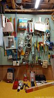 Photo of wall displaying various hardware and hand tools including dustpans, brushes, tapes, and cords hung on hooks.
