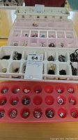 Overview of plastic trays containing various ladies jewelry items including necklaces, earrings, and rings.
