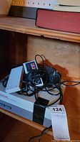 Nintendo Entertainment System (NES) console showing top and front with controllers and power adapter on wooden shelf.
