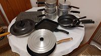 Photo showing assorted pots and pans arranged on a table with lids and handles visible.
