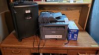 Photo of the Brother printer and toner box placed on a wooden surface beside the black floor shredder.