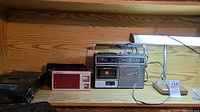 Three vintage radios and a metal lamp on a shelf, seen from front side