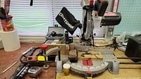 Wide side view of the Craftsman miter saw, showing dust bag, base, handle, and nearby workbench items.