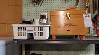 Photo showing the wooden shoe shine kit box next to a plastic basket filled with shoe care accessories such as brushes and polish jars.