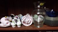 Wide shelf with assortment of stacked and arranged tea cups, plates, small ceramic items, and a glass vase