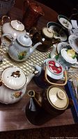 Overview photo showing all eight teapots clustered on a wooden table with other dishware