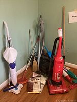 Wide view of red Dirt Devil Featherlite CleanPath vacuum, Kenmore Whispertone canister vacuum, brooms, vacuum bags, and cleaning accessories.