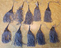 Overview of 10 antique glass beaded tassels arranged on a surface, showing different sizes and bead colors, two tassels with partial separation visible