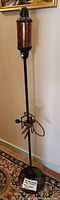 Full view of the floor lamp showing the black metal stand, the mica shade mid-way, and the lamp base with attached cord and plug.