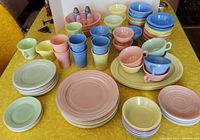 Full lot overview on yellow table showing pastel plates, bowls, cups and shakers