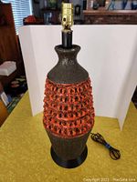 Full view of the large mid-century table lamp showing the textured ceramic body with black and orange colors, topped with a brass socket.