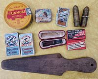 Overview of tobacco-related items including cigarette packs, tin, pipe filters, vintage pipe in case, wooden tool, and brass bullet lighters.