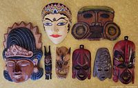 Nine decorative ethnic masks arranged on surface, displaying variety of materials, colors, and styles
